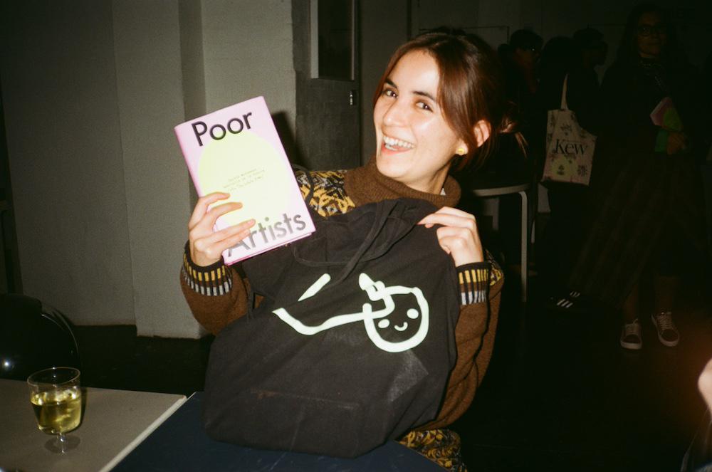 luisa smiles holding the book and a white pube tote bag with the pubemoji logo on it