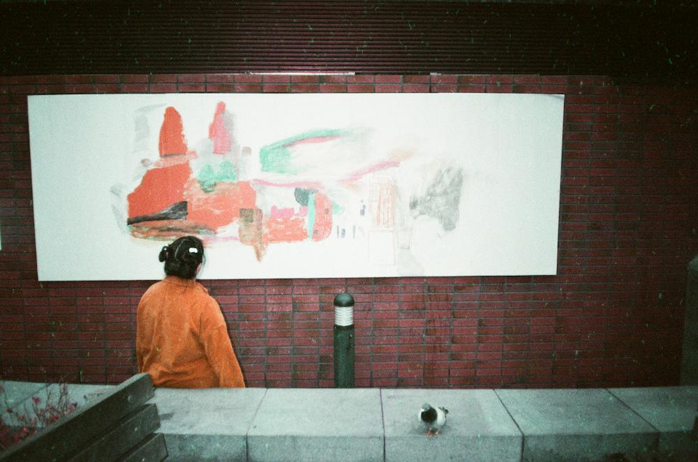 gab with her back to the camera looking at a big white board splashed with abstract colourful shapes nailed to the bricks behind the bluecoat gallery