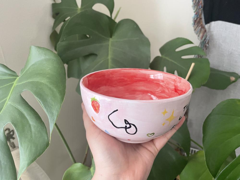 a pale pink bowl with a red centre, on the outside we can see the white pube logo which is of course a pube, some sparkle emojis, a heart, and a strawberry