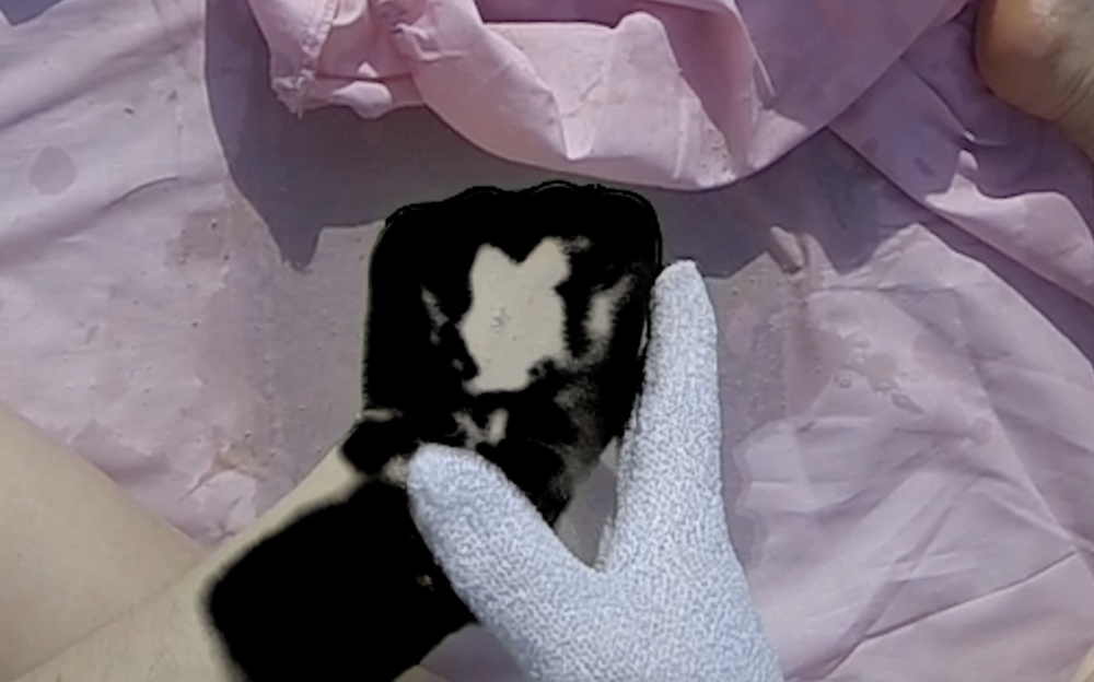 the green spray paint on gabrielle's hand has been keyed out so it is a deep empty digital black, and she is wearing an exfoliation glove on the other hand, using it to scrub the black ie. the neon green off it