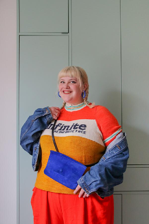 lydia smiles wearing a jumper with a zipped colour and a stripe across the chest with the words infinite
