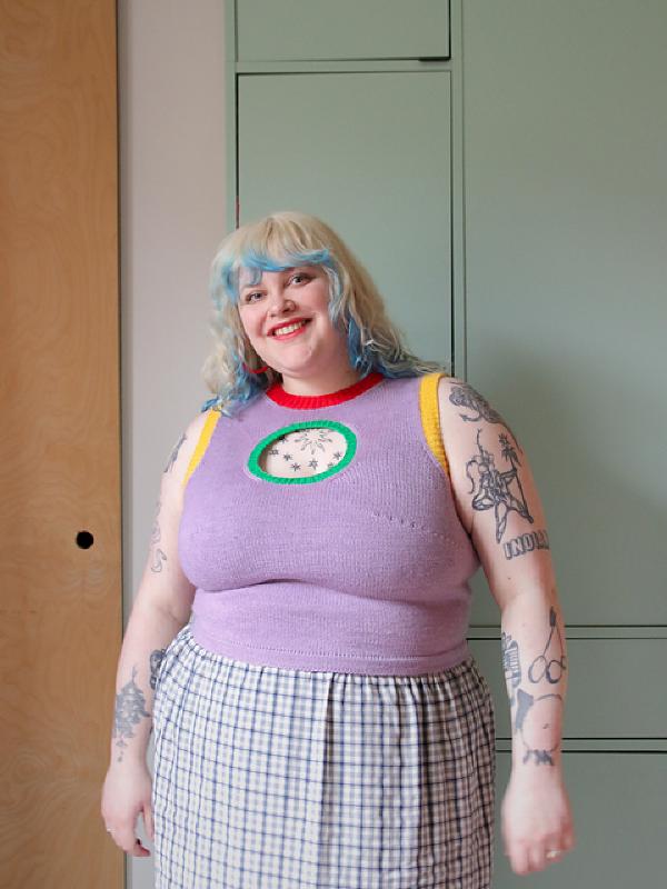 lydia wears a full coverage tank top knitted with different colours and a hole over the centre of the chest