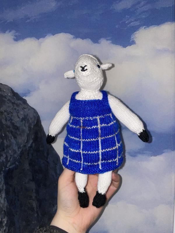 gab holds up a knitted sheep plush teddy in a dress