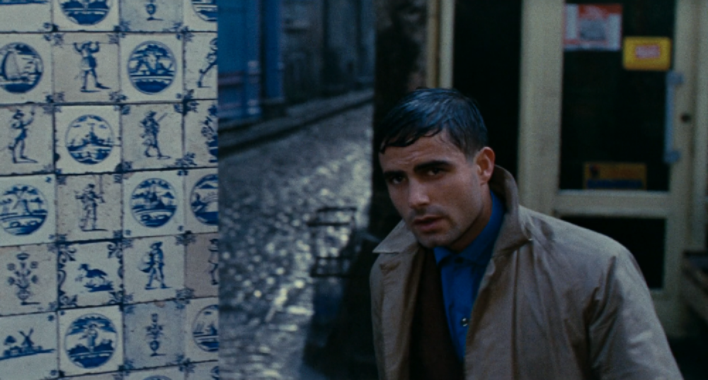 Nino in the rain, hair all wet and flat, next to white tiles painted with blue motifs