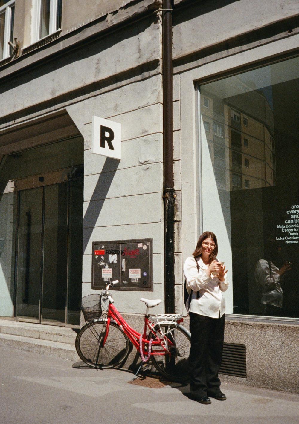 lucija klauž standing outside of a gallery next to a red bike