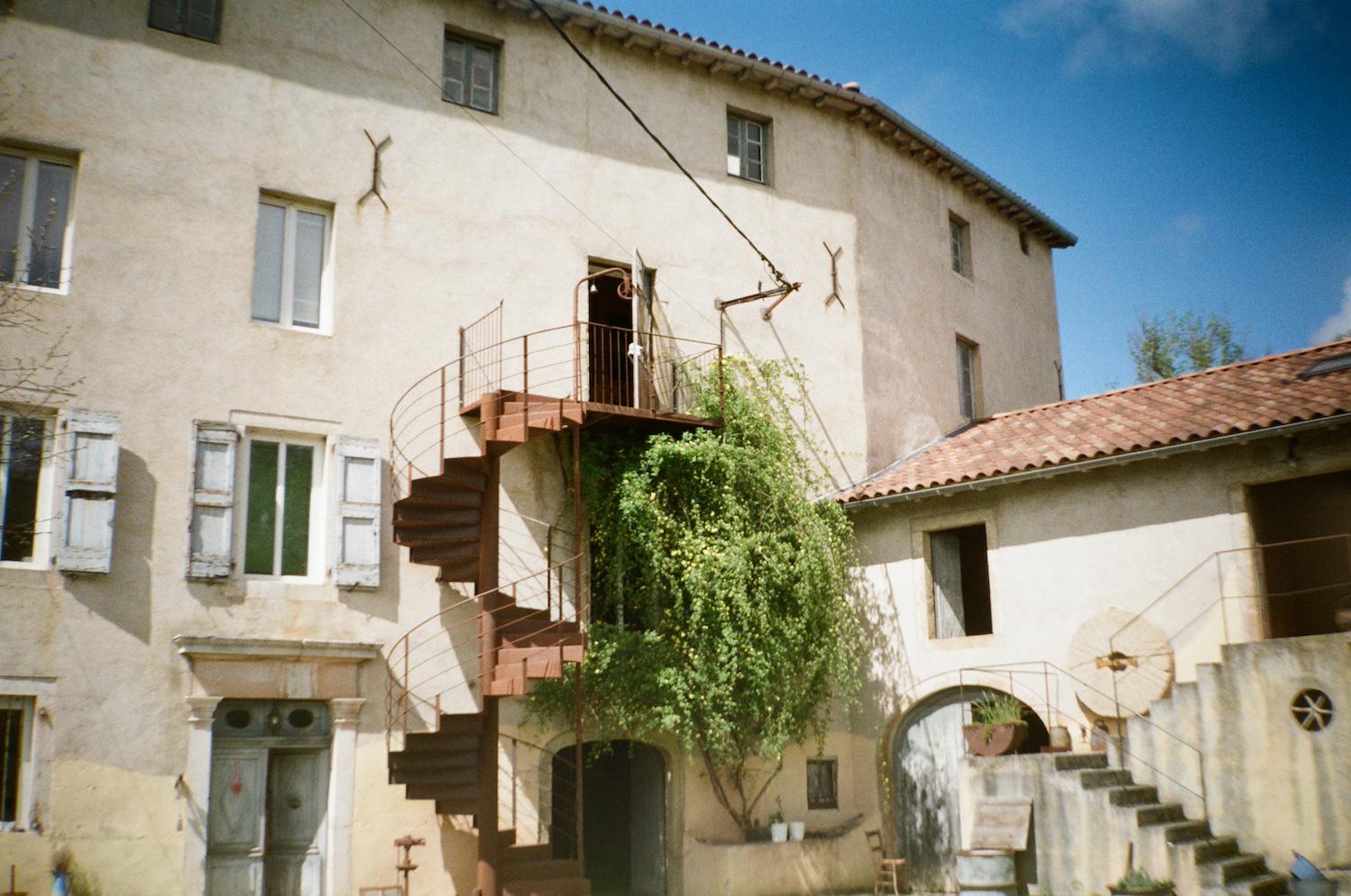 a 4 storey mill with shuttered windows and two staircases on the facade, one a spiral staircase up to the third floor, and another to the barn-like event space on another wing of the house
