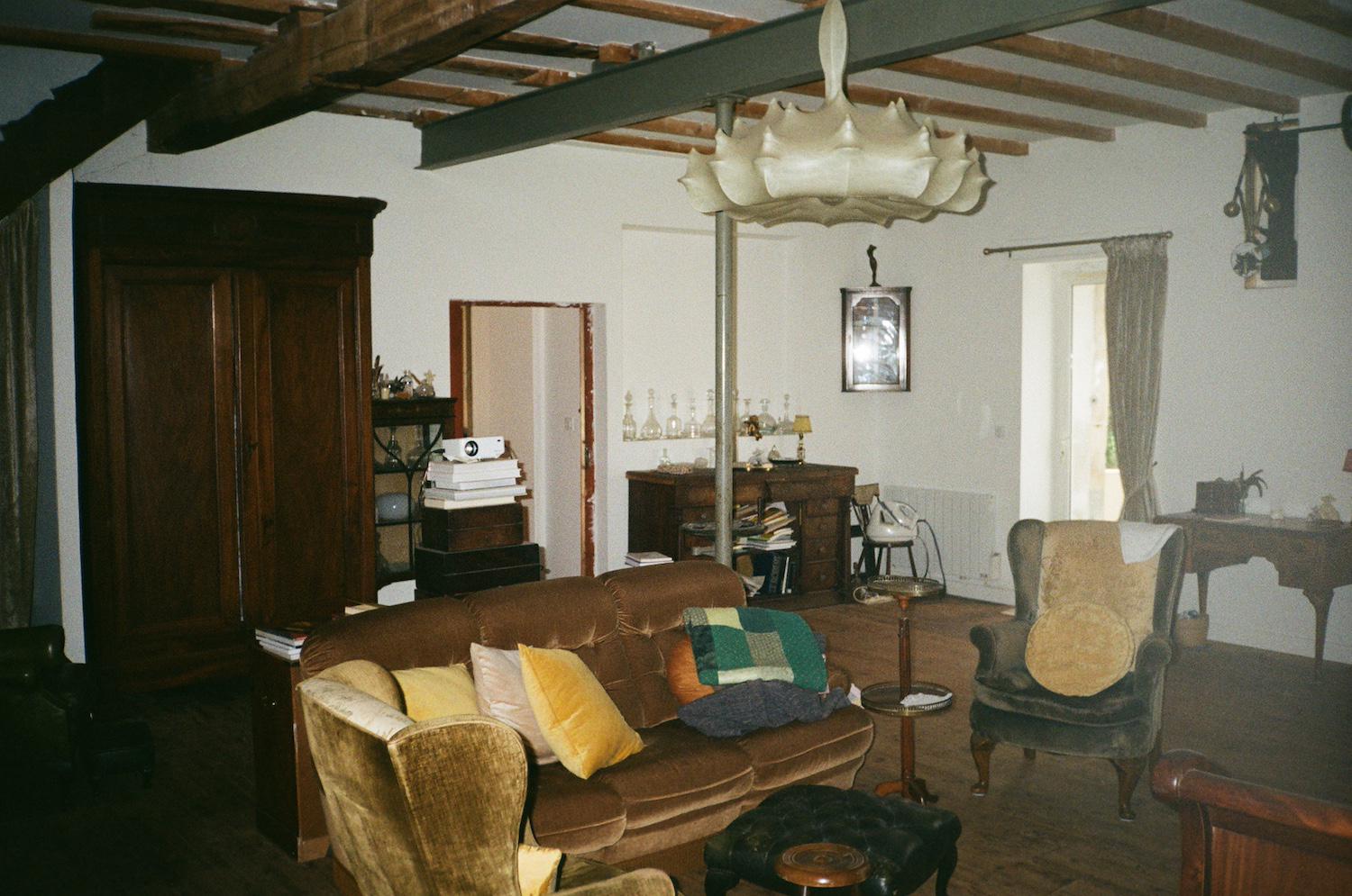 velvet furniture and a chandelier that has been covered in fabric in a room with a big warddrobe, a projector, and exposed ceiling beams