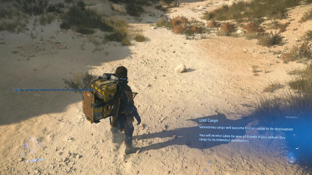 The player view looking at Sam standing in rocky terrain in Death Stranding 2 with a notification about what to do when you find lost cargo