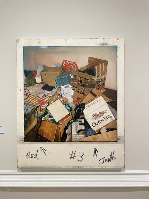 brian bishop's polaroid painting, a tall thing on the wall, showing a junky pile of shit in someone's house like an empty champagne box, and a basket, and a striped mattress