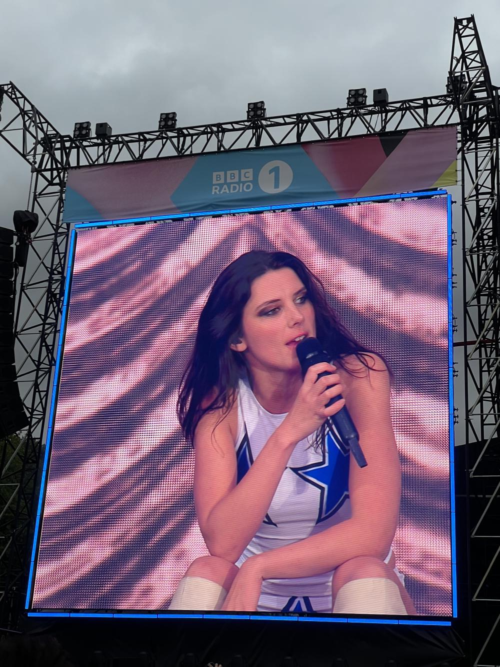 ellie roswell on a big screen sat down singing