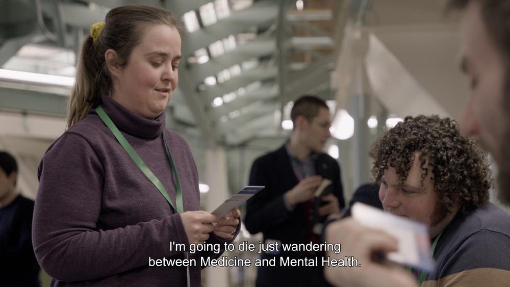 a woman with a lanyard looked down at the card on it and says i'm going to die just wandering between medicine and mental health
