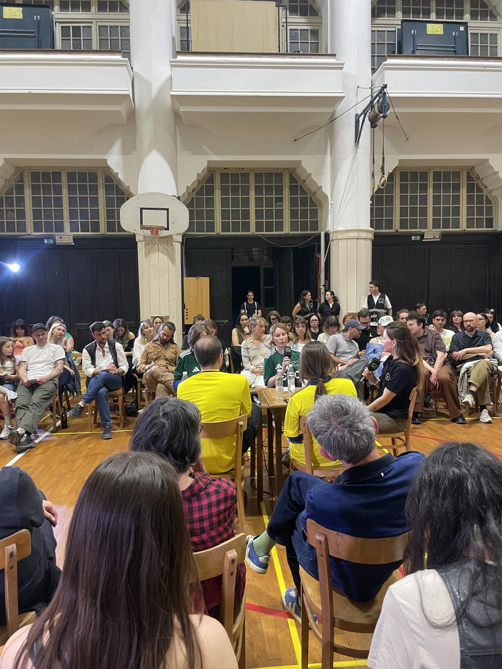 critics gathered around a table in the middle of a sports hall with the audience flanking them