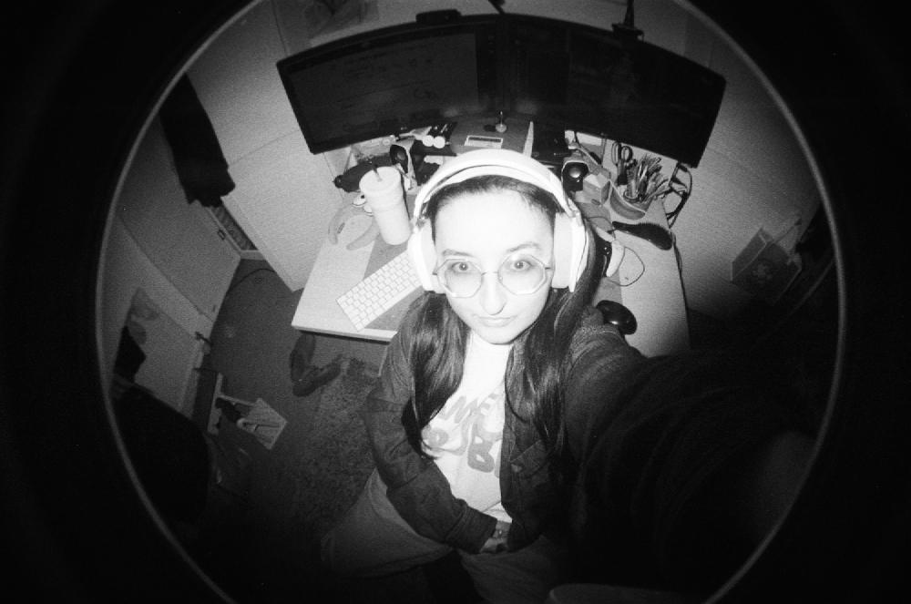 gab taking a selfie at her desk with a fisheye film camera in black and white film, magic keyboard visible to her side