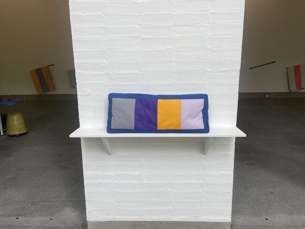 a cushion on a small shelf with grey purple yellow and lilac squares across the middle section