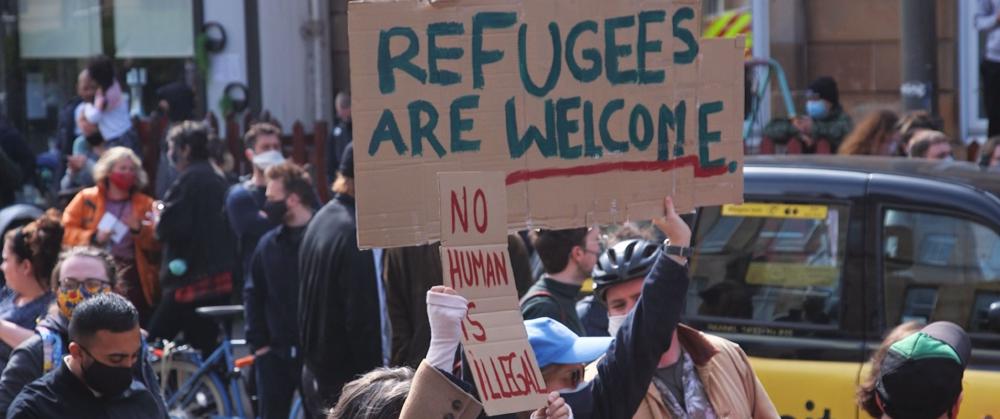 protesters at kenmure st hold cardboard signs saying refugees are welcome and no human is illegal